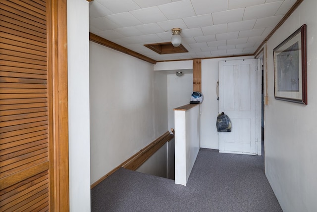 hallway featuring dark colored carpet, ornamental molding, and an upstairs landing