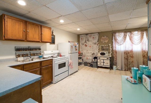 kitchen with white appliances, a drop ceiling, brown cabinets, light countertops, and a sink