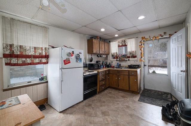 kitchen featuring electric stove, light countertops, brown cabinetry, freestanding refrigerator, and black microwave