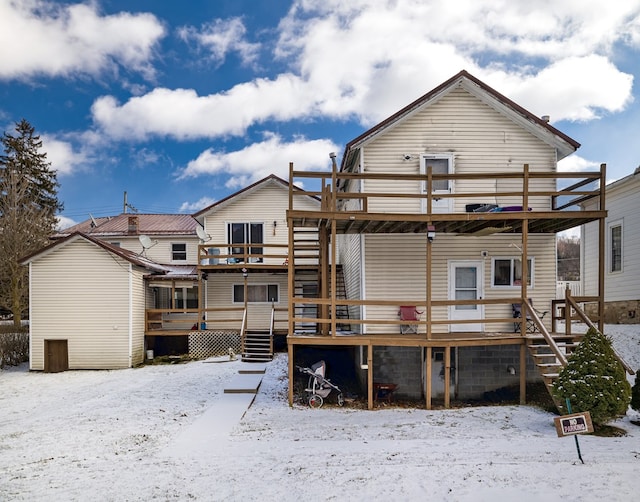 snow covered back of property featuring stairs and a wooden deck