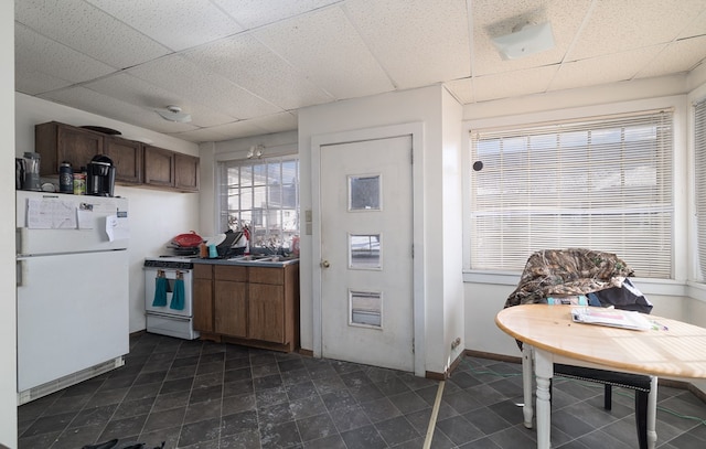 kitchen with white appliances, a drop ceiling, and baseboards