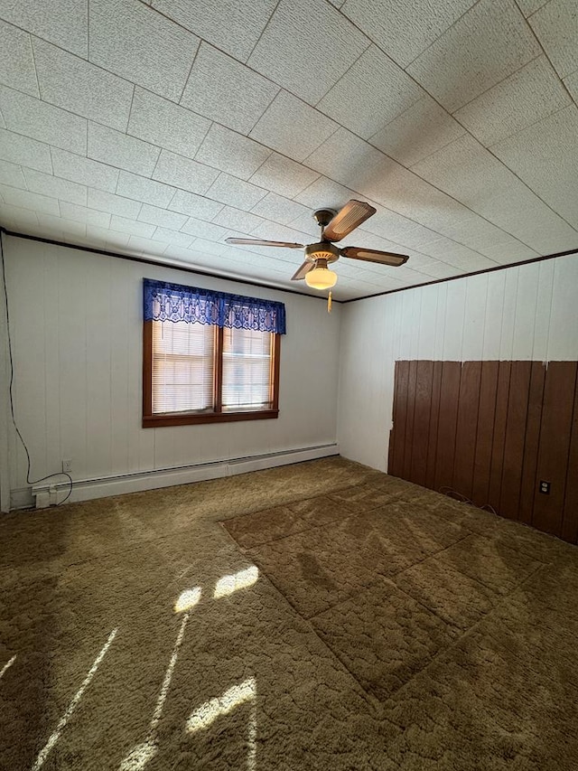 empty room with ceiling fan, a baseboard heating unit, wood walls, and carpet flooring