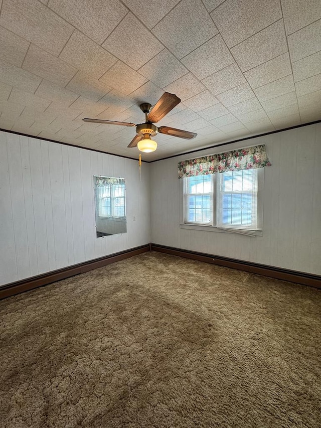 empty room with ceiling fan, carpet floors, and wooden walls