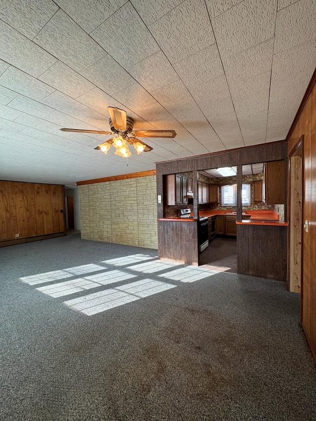 unfurnished living room featuring ceiling fan, dark carpet, and wooden walls