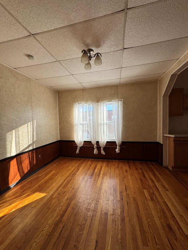 empty room with a paneled ceiling, wood walls, and hardwood / wood-style flooring