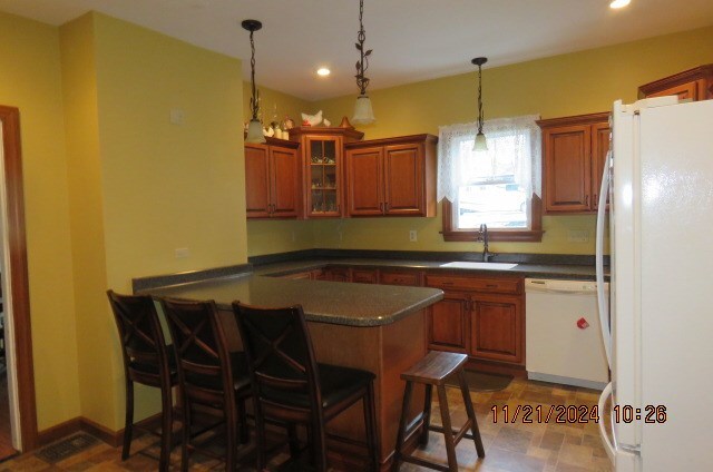 kitchen featuring a breakfast bar, white appliances, sink, hanging light fixtures, and kitchen peninsula