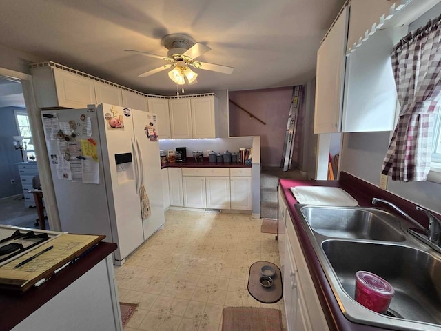 kitchen featuring a sink, white refrigerator with ice dispenser, white cabinets, light floors, and ceiling fan