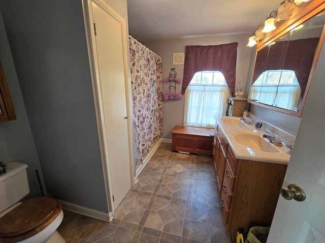 bathroom featuring double vanity, toilet, baseboards, and a sink