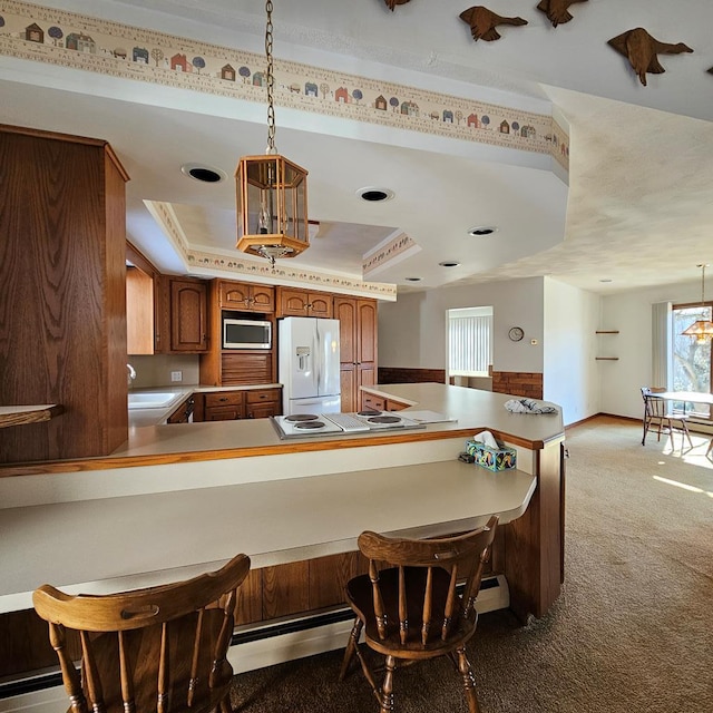 kitchen featuring light carpet, white appliances, decorative light fixtures, and a raised ceiling