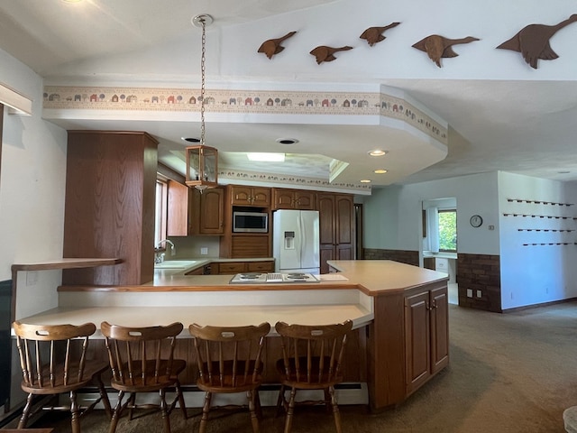 kitchen featuring pendant lighting, sink, dark colored carpet, kitchen peninsula, and white appliances