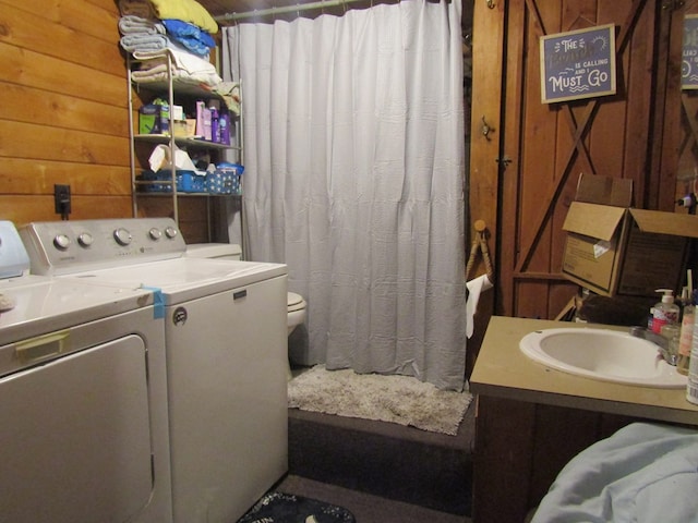 clothes washing area with washer and clothes dryer, wood walls, and sink