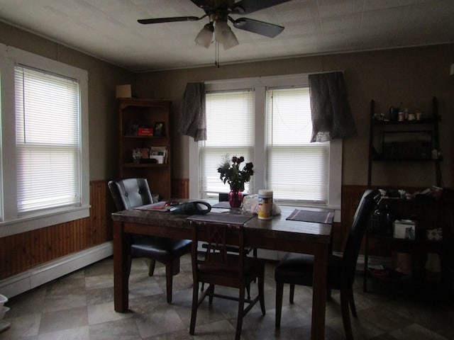 dining room with wood walls, plenty of natural light, ceiling fan, and a baseboard radiator