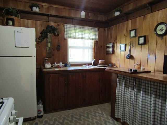 kitchen with range, white refrigerator, and wood walls