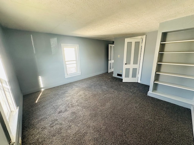 unfurnished bedroom with a textured ceiling and dark colored carpet