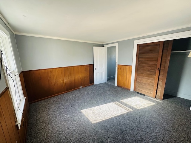 unfurnished bedroom with wooden walls, a closet, dark carpet, and ornamental molding