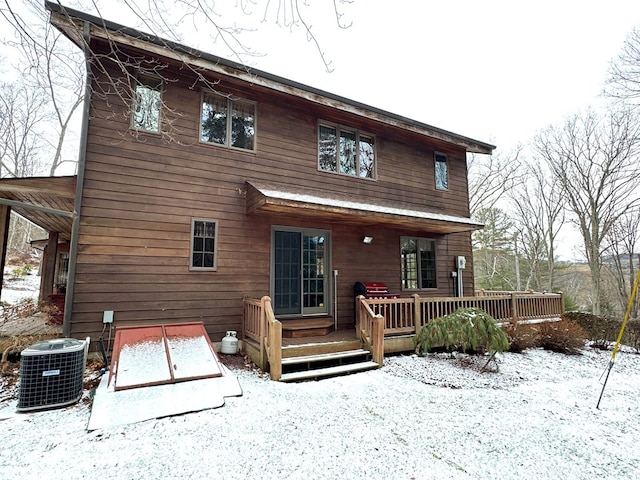 snow covered back of property with central air condition unit and a wooden deck