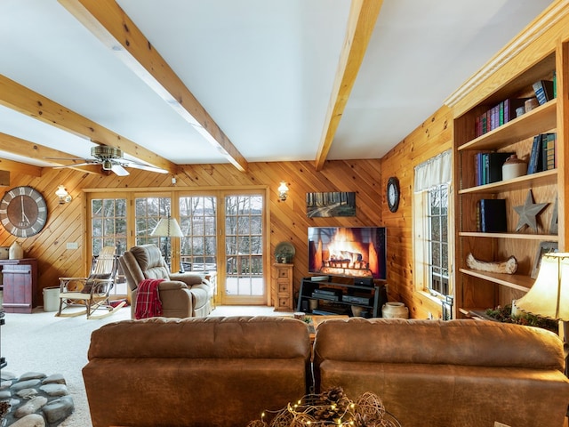 carpeted living room featuring beam ceiling, ceiling fan, and wooden walls