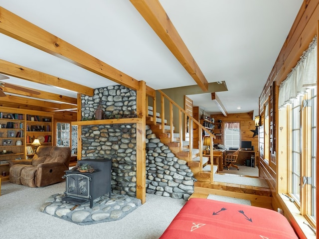 carpeted living room featuring beamed ceiling, wooden walls, built in features, and a wood stove