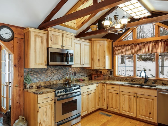 kitchen with appliances with stainless steel finishes, vaulted ceiling with beams, a notable chandelier, dark stone counters, and sink