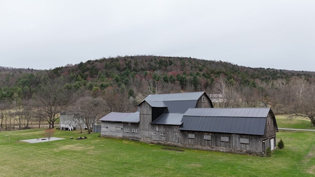 exterior space with a barn, a wooded view, metal roof, a gambrel roof, and a lawn