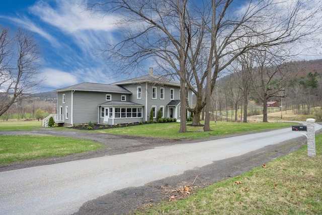 view of front of house featuring a front yard, a sunroom, driveway, and a chimney