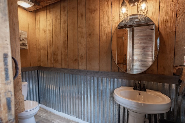 half bath featuring wood walls, a sink, toilet, and wood finished floors