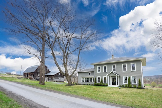 colonial-style house with a barn, a chimney, and a front lawn