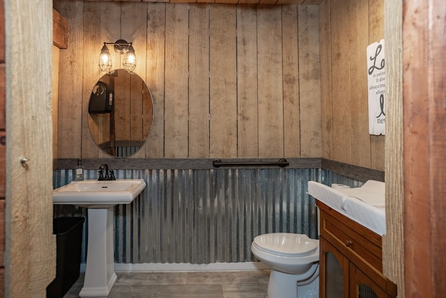 half bathroom featuring a sink, wood walls, toilet, and wood finished floors