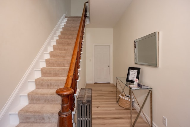 staircase with radiator, wood finished floors, and baseboards