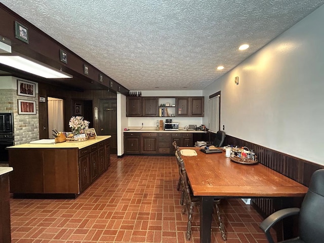 kitchen with a textured ceiling, dark brown cabinetry, oven, and sink