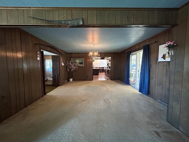 unfurnished dining area with wood walls, carpet floors, and a notable chandelier