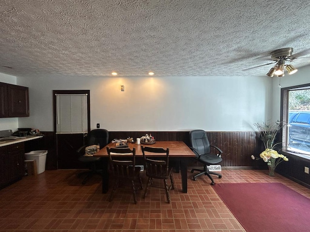 dining space with a textured ceiling, ceiling fan, and wooden walls