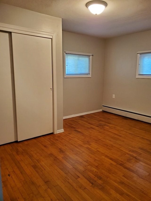 unfurnished bedroom with multiple windows, wood-type flooring, baseboard heating, and a closet