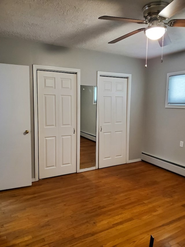 unfurnished bedroom featuring a textured ceiling, two closets, ceiling fan, a baseboard radiator, and hardwood / wood-style floors