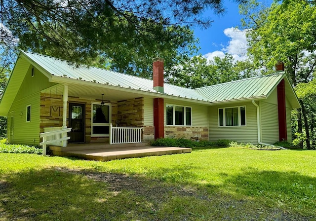 rear view of property featuring covered porch, a chimney, stone siding, a lawn, and metal roof