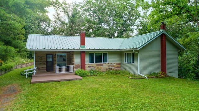 rear view of house featuring covered porch, a chimney, metal roof, a yard, and stone siding