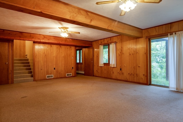 carpeted empty room featuring visible vents, baseboard heating, wood walls, and stairway