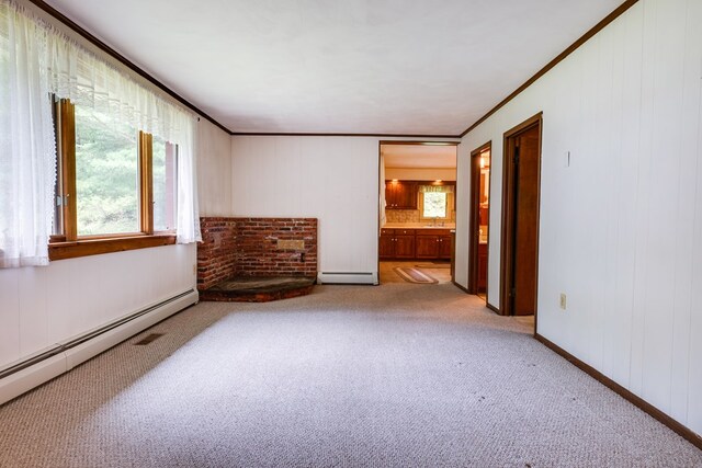 carpeted spare room with a baseboard heating unit, baseboards, and crown molding