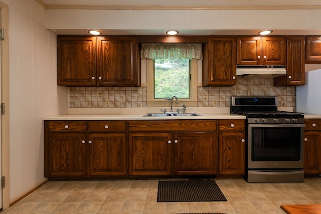 kitchen with backsplash, under cabinet range hood, light countertops, stainless steel gas range, and a sink