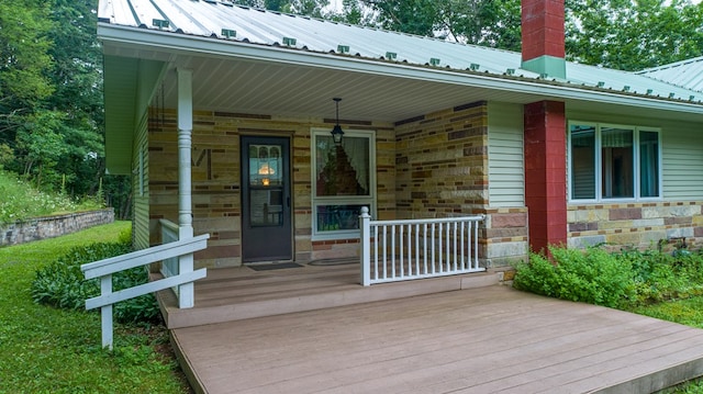 doorway to property with metal roof, stone siding, covered porch, and a chimney