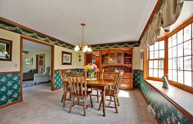 carpeted dining room featuring wainscoting, visible vents, a chandelier, and crown molding