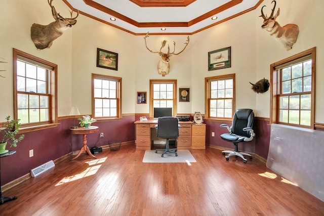 office space with hardwood / wood-style flooring, a towering ceiling, baseboards, ornamental molding, and visible vents