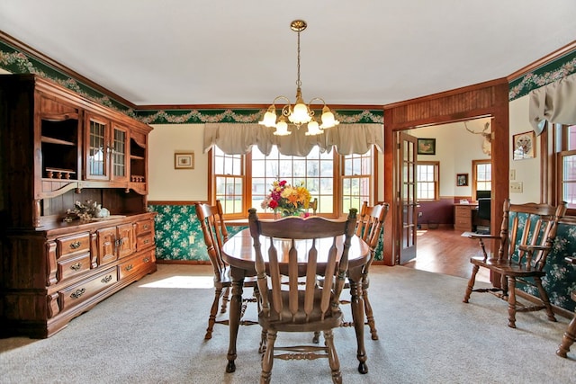 carpeted dining room featuring a healthy amount of sunlight, crown molding, a wainscoted wall, and an inviting chandelier