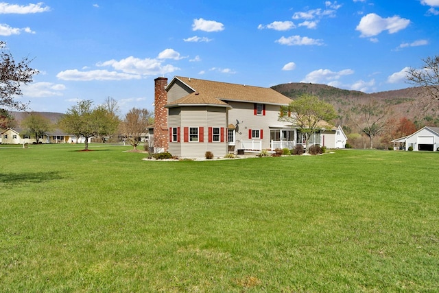 rear view of house with a chimney, a mountain view, and a yard