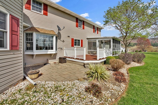 rear view of house featuring a patio area, a sunroom, a lawn, and a deck