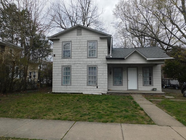traditional home featuring roof with shingles, covered porch, and a front lawn