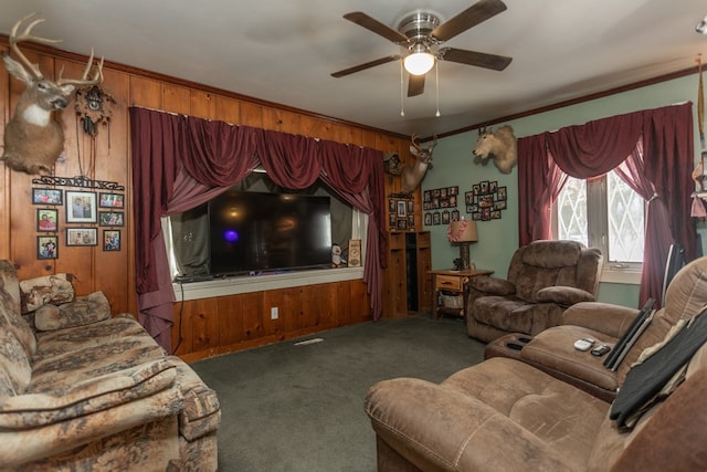 living room featuring wooden walls, dark colored carpet, ceiling fan, and ornamental molding