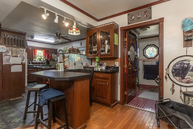 kitchen with ceiling fan, sink, a kitchen breakfast bar, light hardwood / wood-style flooring, and ornamental molding