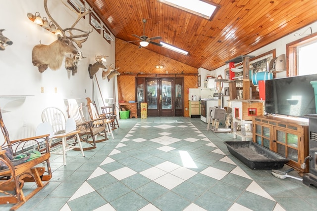 interior space with french doors, a skylight, ceiling fan, wooden walls, and high vaulted ceiling