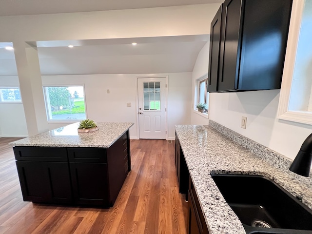 kitchen with light stone counters, wood finished floors, dark cabinets, and a sink